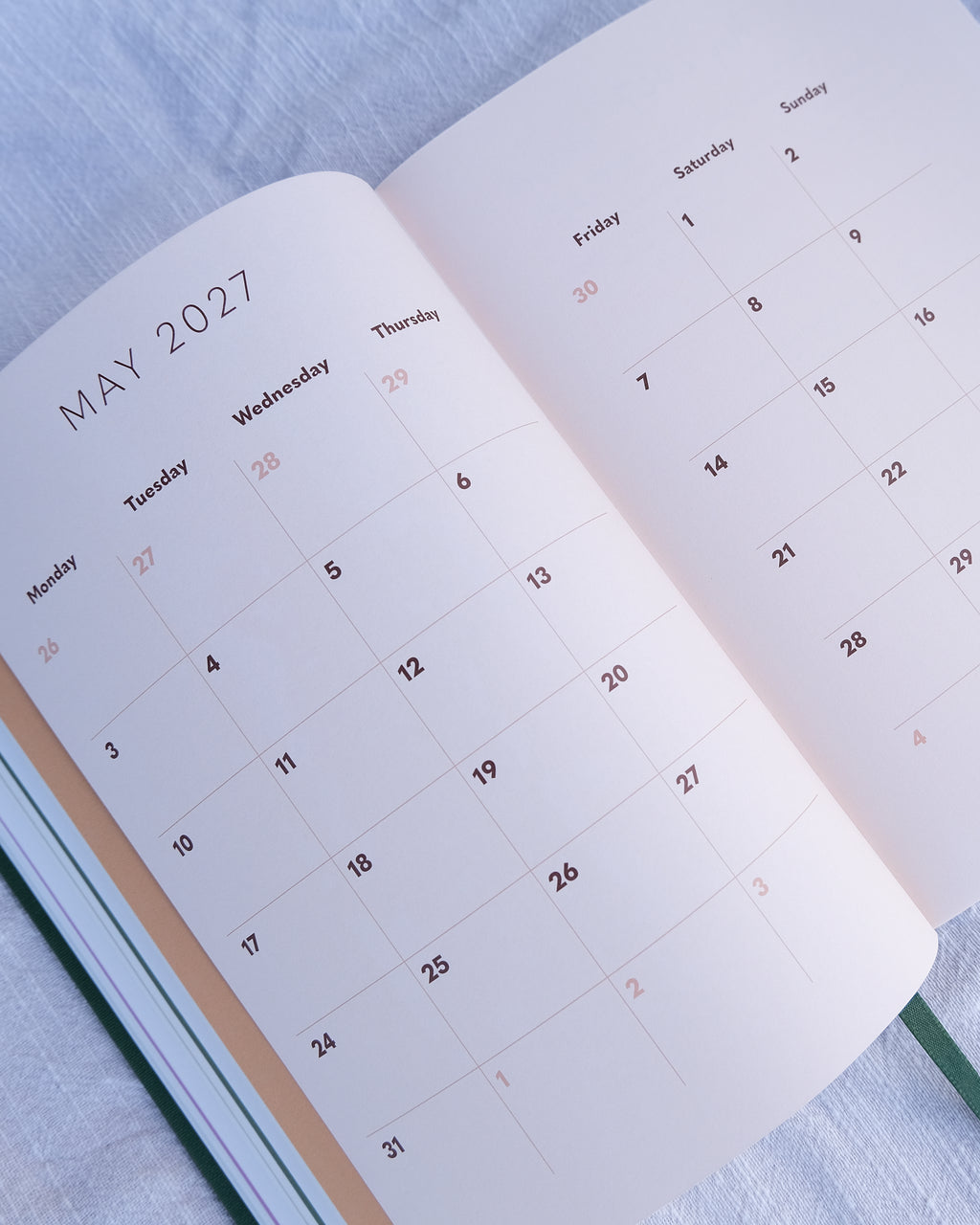 An open planner showing May 2027 on the left page and a weekly calendar from the 1st on the right page, photographed on a light textured fabric background.