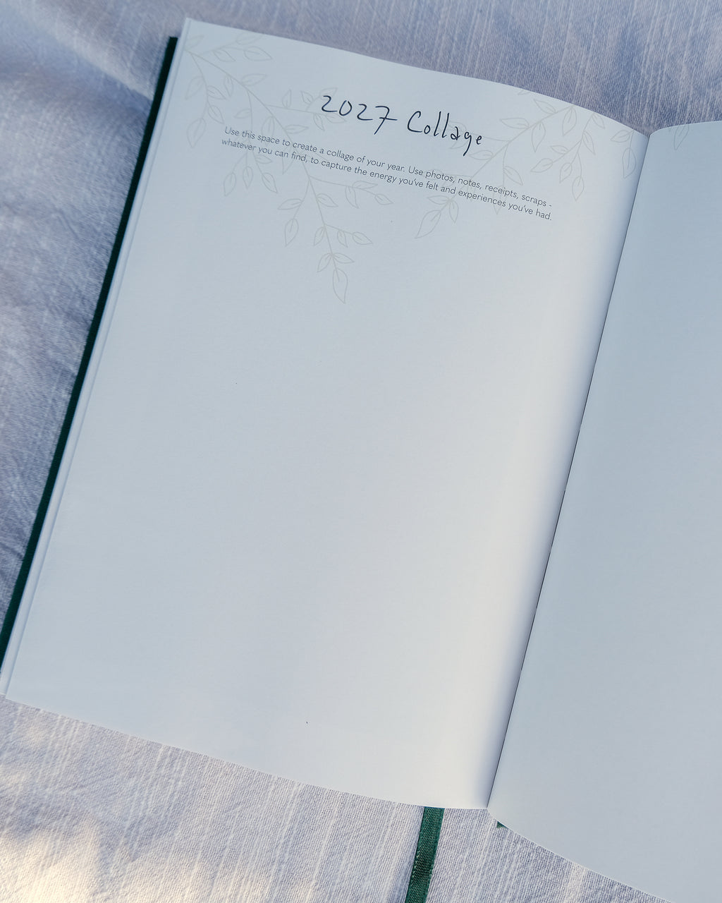 An open planner showing a blank page with the handwritten heading '2027 College' and a small faint line drawing, placed on a light blue textured fabric surface.